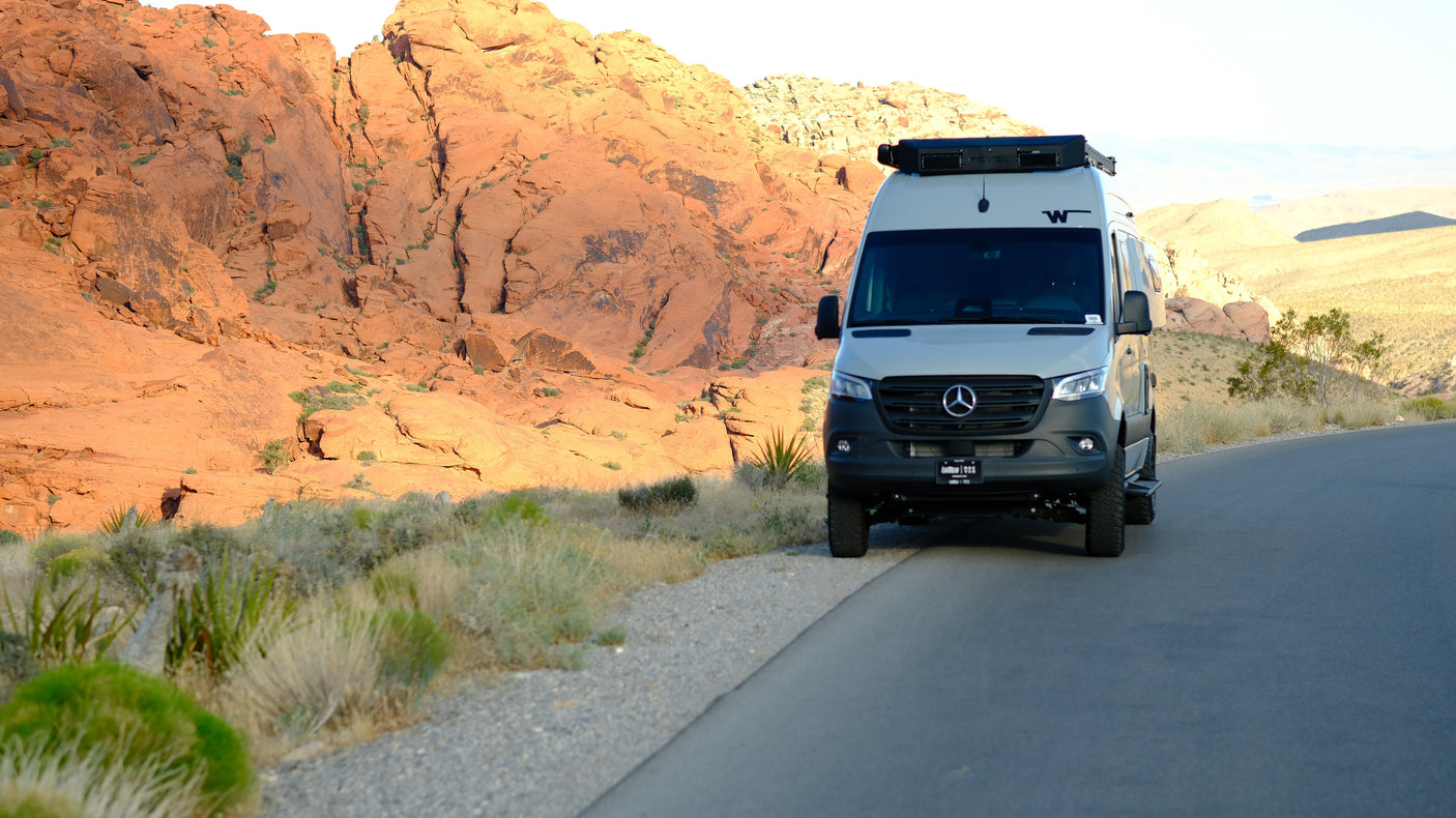 An RV rental Mercedes Sprinter camper van on a desert road with stunning red rock formations. Perfect for an adventure!