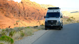 An RV rental Mercedes Sprinter camper van on a desert road with stunning red rock formations. Perfect for an adventure!