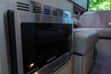 A sleek, stainless steel CONTOURE microwave oven in the modern kitchen area of an rv rental, with plush seating visible in the background.