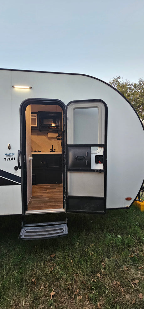 Explore this Braxton Creek 17BH rv rental, showcasing its open door, steps, and compact interior kitchen setup.