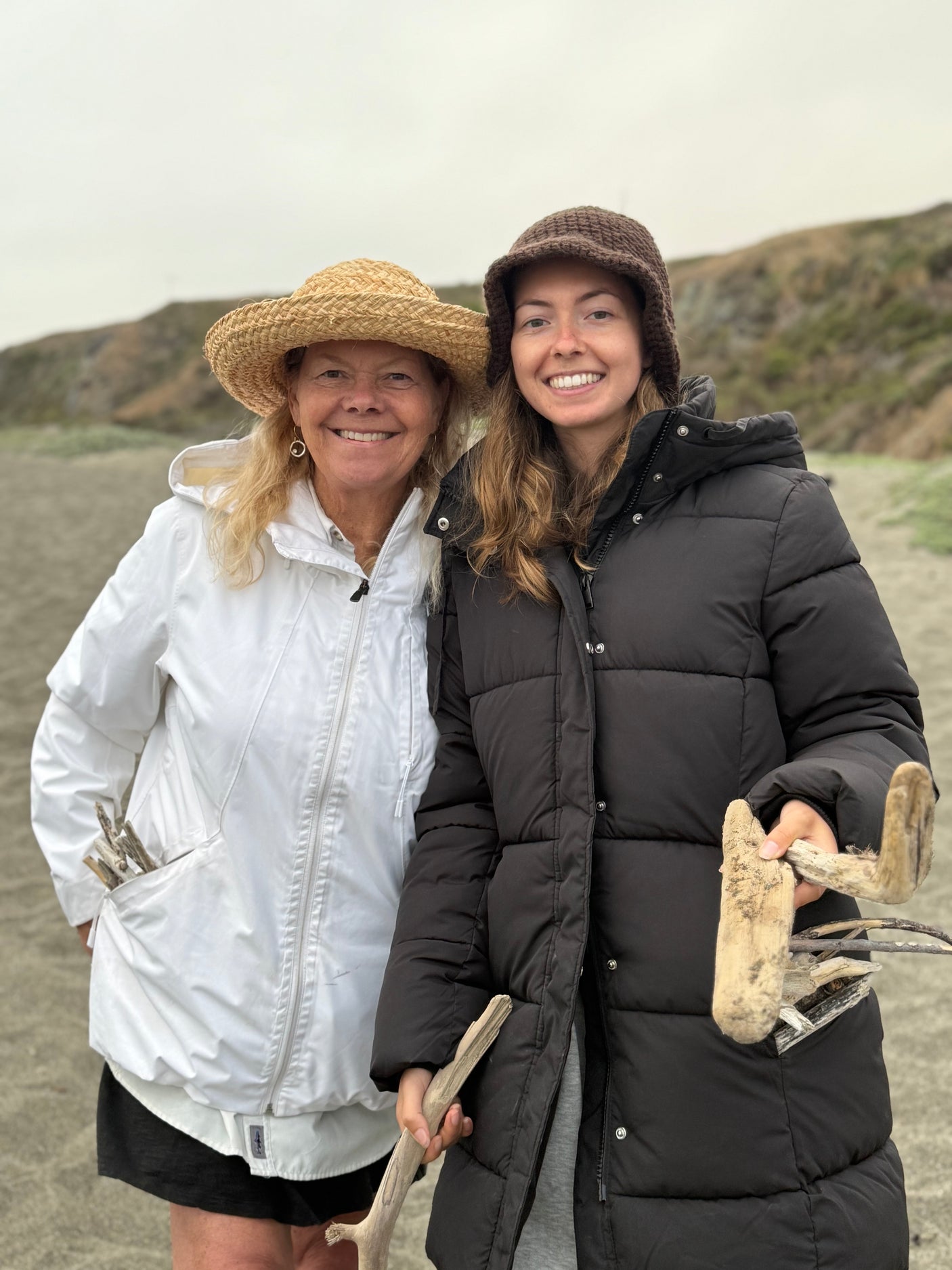 Smiling women with collected driftwood on a beach, enjoying their RV rental vacation.