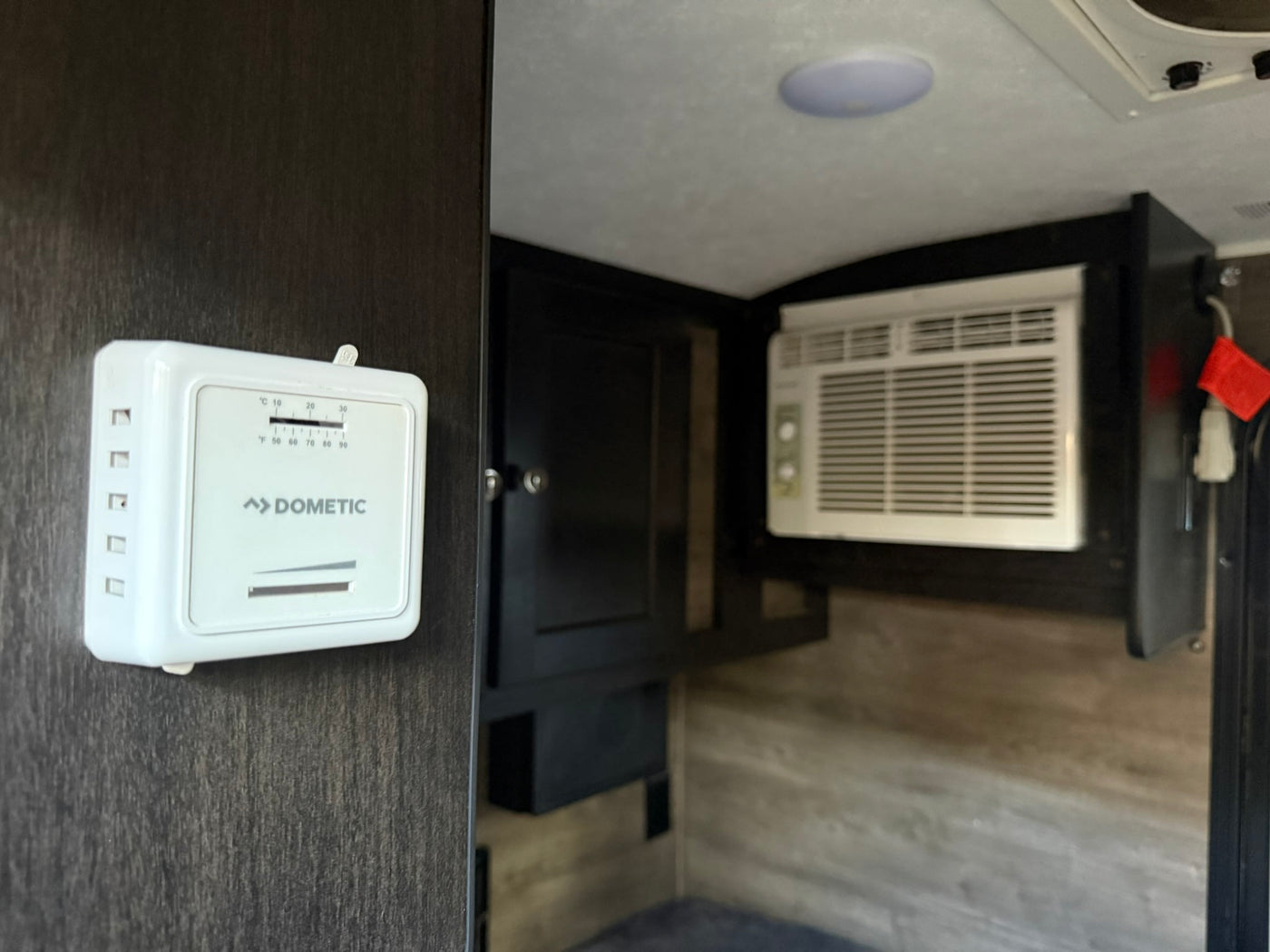 RV rental interior: A white Dometic thermostat is mounted on a dark wall, next to a compact AC unit. — photo 8
