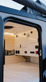Cozy RV rental interior shows a clean bed, warm LED lighting, and a practical control panel with storage, ready for comfortable travel.