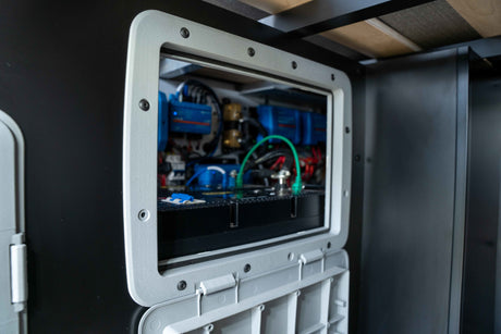 An open access panel inside an RV rental reveals the essential electrical power system with blue components and wiring.