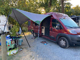 A red rv rental camper van with a large tarp awning set up at a shady campsite, ready for outdoor living.