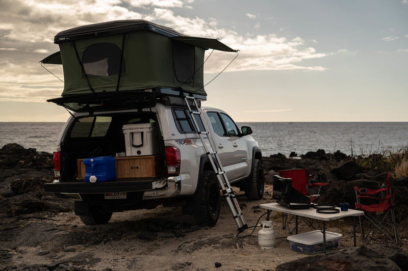 Explore with this RV rental: White Toyota pickup with rooftop tent, ladder, and full camp setup on a rocky beach. — photo 2