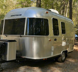 This shiny Airstream RV rental is perfect for a cozy camping adventure, nestled among tall trees in the outdoors.