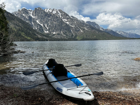 An inflatable kayak rests on the rocky shore of a majestic mountain lake, ideal for an RV rental outdoor adventure.