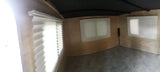 Interior of an RV rental: light wood walls, pleated window blinds, and seating. A small control panel is visible.