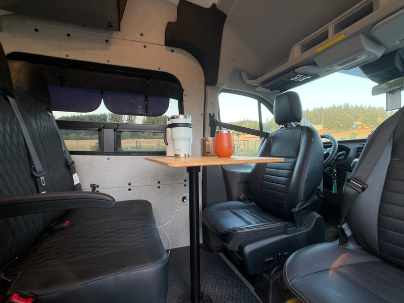 Cozy RV rental interior featuring black seats, a wooden table with mugs, and scenic window views. Perfect mobile setup! — photo 3