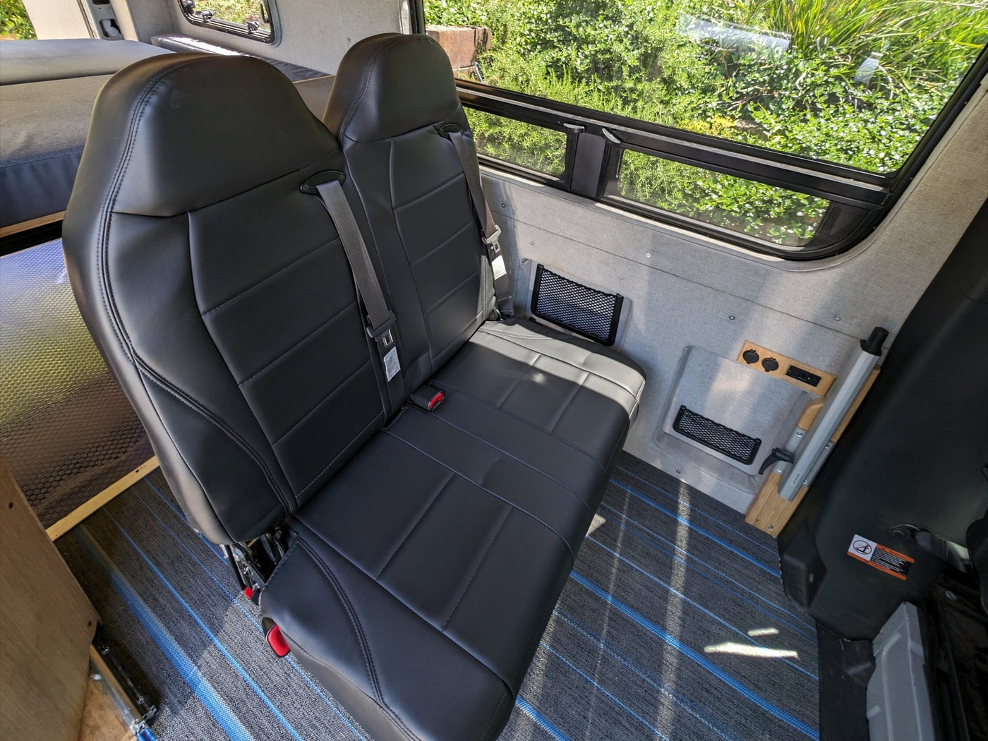  parked with a dark car. Background shows greenery and a building.|Bright rv rental camper van interior. Features black leather seats — photo 7