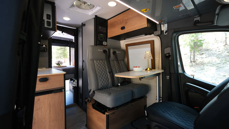 This rv rental's interior offers comfy passenger seats, a dining table, kitchenette, and bedroom for adventure travel.