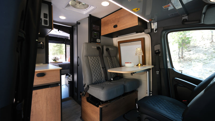 This rv rental's interior offers comfy passenger seats, a dining table, kitchenette, and bedroom for adventure travel.