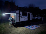 Enjoying an RV rental experience: a man cooks dinner outside a Clipper RV at a dark campsite, with a Jeep nearby.