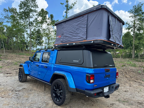 This blue Jeep Gladiator pickup, with a SmartCap and Roofnest rooftop tent, offers an adventurous alternative to rv rental camping.