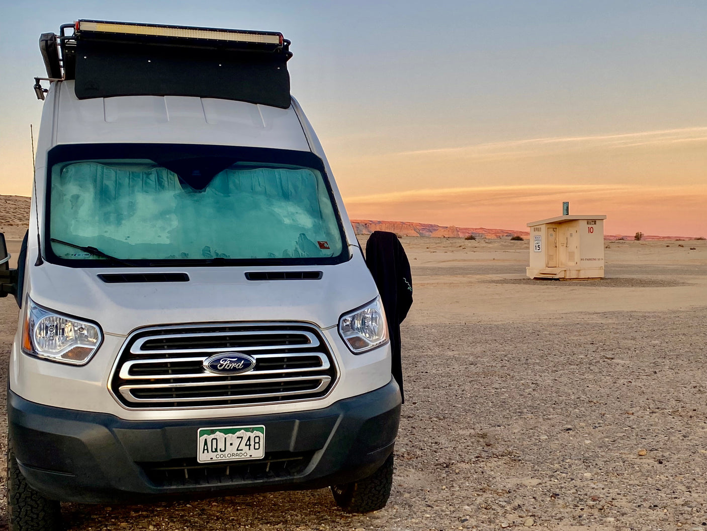 White Ford RV rental van parked at sunset in a desert landscape near a facility building. Ideal for outdoor travel.