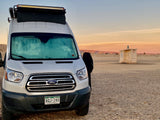 White Ford RV rental van parked at sunset in a desert landscape near a facility building. Ideal for outdoor travel.