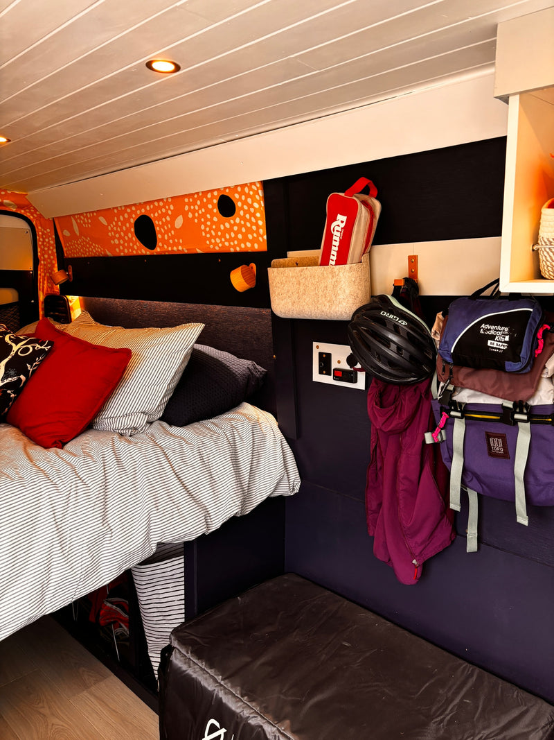 RV rental's inviting bedroom: comfy bed, vibrant decor, and efficient wall storage for a bike helmet & travel essentials. — photo 5
