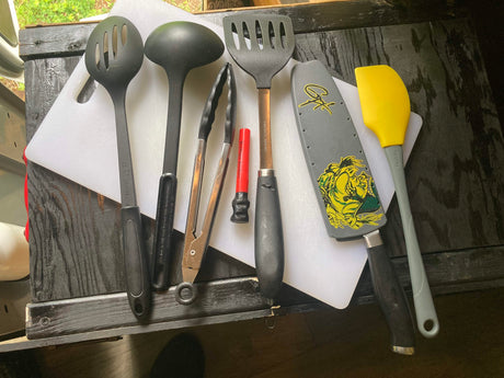Essential kitchen tools for your RV rental adventure: slotted spoon, ladle, tongs, spatulas, and a knife on a cutting board.