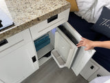 Compact RV rental kitchenette: A hand opens the built-in mini-fridge in white cabinetry with a granite counter.