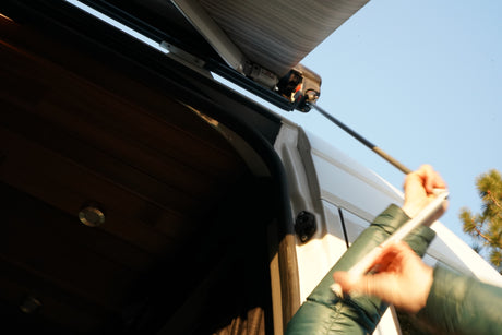 Extending the awning on your rv rental! Hands use a pole to set up the camper's outdoor shade under a blue sky.
