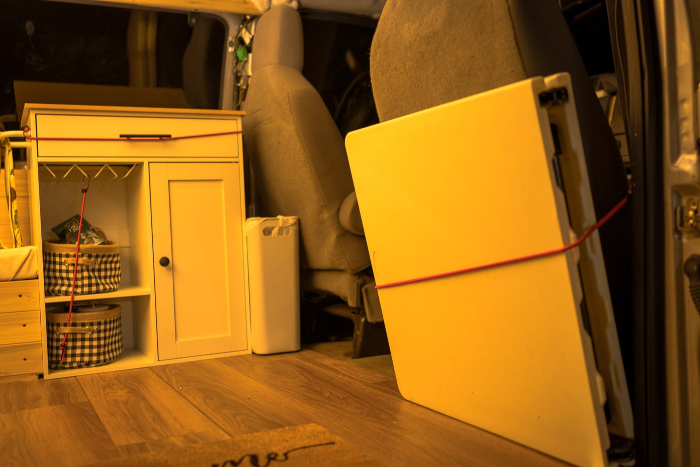 Cozy rv rental interior: light wood floor, white storage unit with checkered baskets, and a secured upright panel for organized mobile living.
