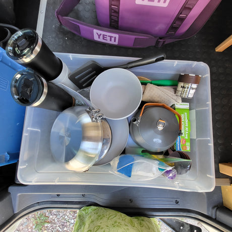RV rental kitchen gear: pots, pans, cups, spices, & cooking tools neatly packed in a clear bin for camping cooking.