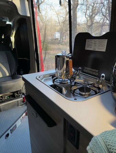 Inside an RV rental: a gleaming percolator brews on the two-burner stove in a compact kitchen, with an outdoor view. — photo 6