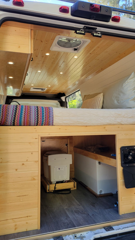 This RV rental features a comfortable bed, custom wood interior, pull-out toilet, and ample under-bed storage with water tank.