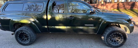 Dark green Toyota Tacoma pickup truck with a camper shell & off-road tires, perfect for an RV rental adventure.