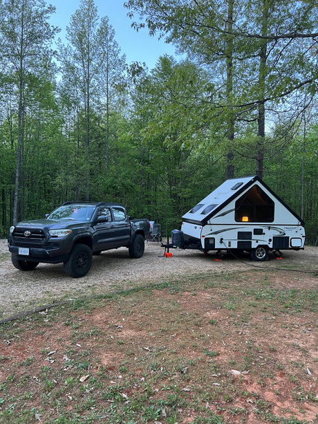 RV rental truck towing an A-frame camper at a wooded campsite, ideal for outdoor adventures.
