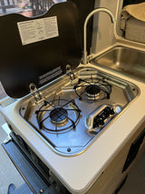 An RV rental's stainless steel kitchen featuring a 2-burner gas stove, sink, and faucet for on-the-go cooking.