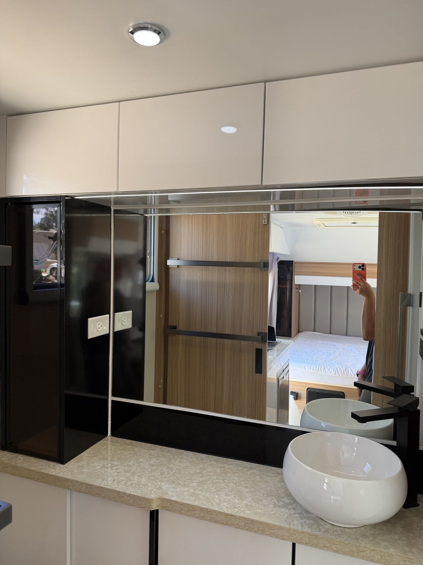 Bathroom vanity with a white vessel basin, black mixer tap, full-width mirror reflecting the bedroom, overhead cabinets and the shower enclosure alongside — photo 15