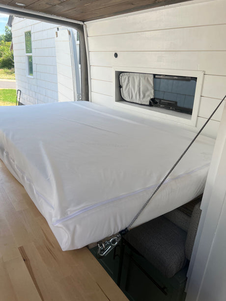 This RV rental features a cleverly designed lift-up bed with white mattress, revealing storage & seating, maximizing camper space.