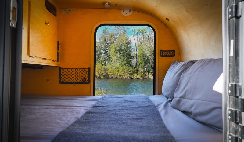 Inside this cozy RV rental: a comfortable bed offers serene river and forest views from the large window. Perfect for glamping. — photo 3