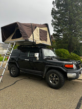 Black FJ Cruiser with a brown rooftop tent deployed, ladder extended. Perfect for an adventure rv rental.