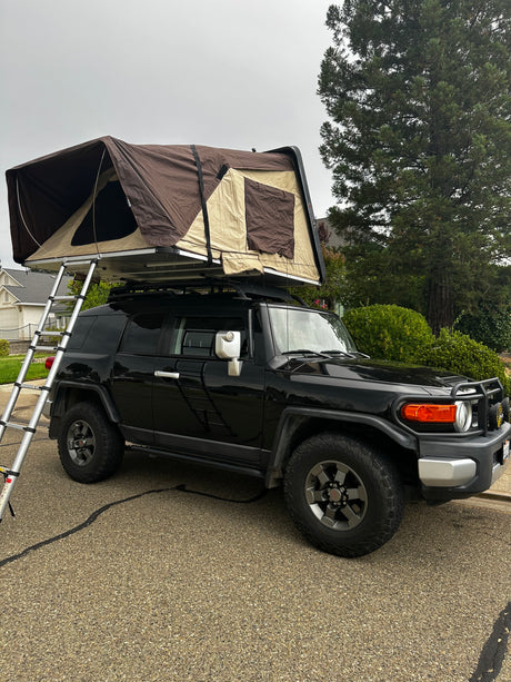 Black FJ Cruiser with a brown rooftop tent deployed, ladder extended. Perfect for an adventure rv rental.