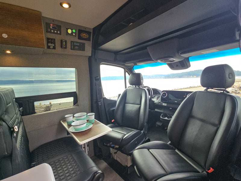 Storyteller RV rental interior: front seats, table with dishes, and panoramic ocean views. Ready for adventure! — photo 5