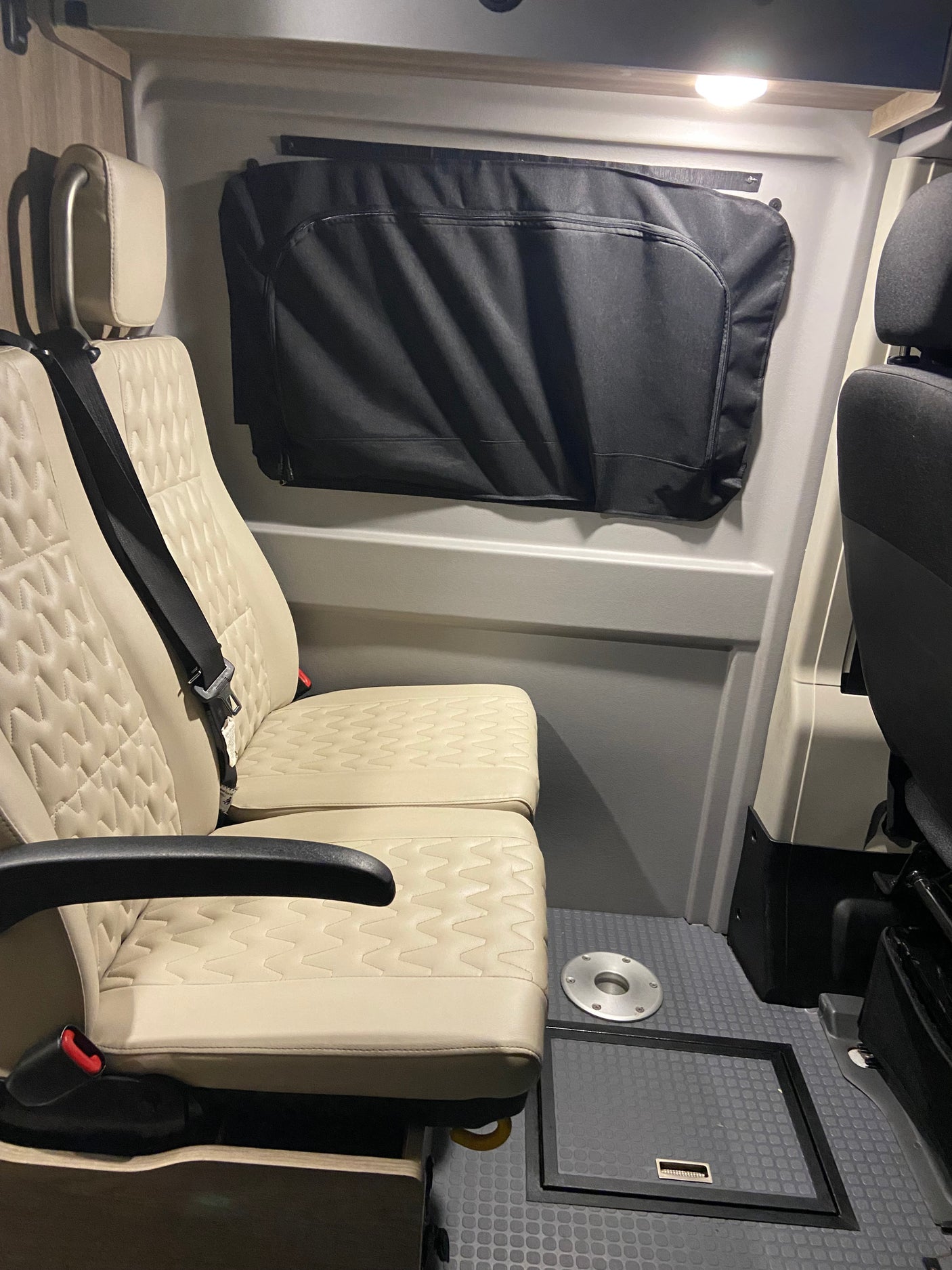 RV rental interior: two beige passenger seats, window cover, and a versatile floor with table base & storage hatch.