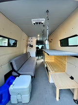 Explore this RV rental's spacious camper van interior, showcasing a long bench, portable toilet, and pull-out table/counter.