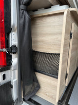 RV rental interior: wood-look storage unit with net pocket & mesh screen near the vehicle's rear door.