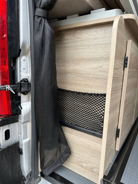 RV rental interior: wood-look storage unit with net pocket & mesh screen near the vehicle's rear door.