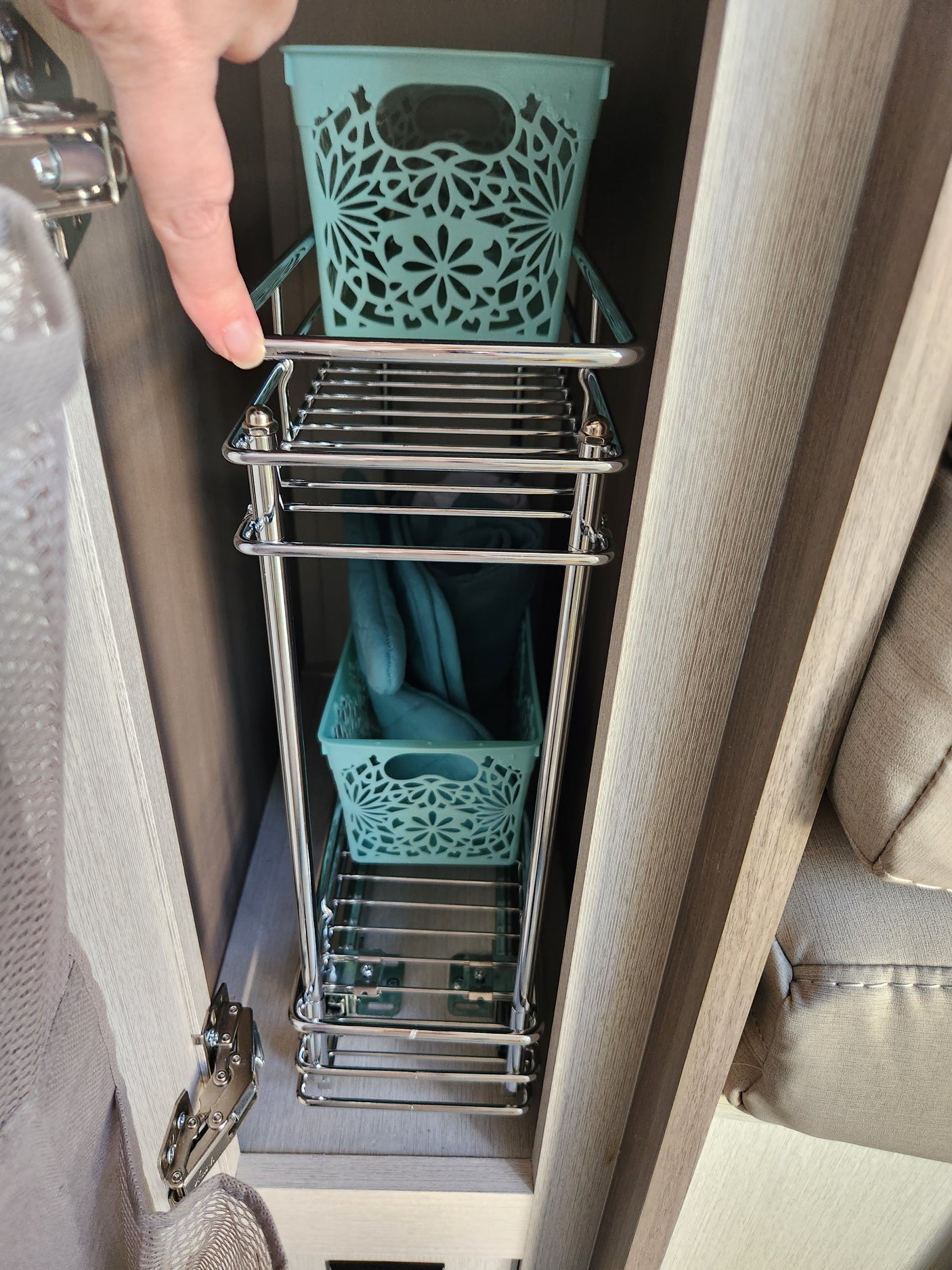 RV rental: Finger points to a chrome pull-out rack with teal decorative bins, maximizing under-cabinet storage.