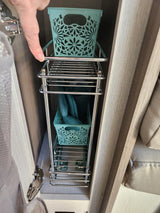 RV rental: Finger points to a chrome pull-out rack with teal decorative bins, maximizing under-cabinet storage.