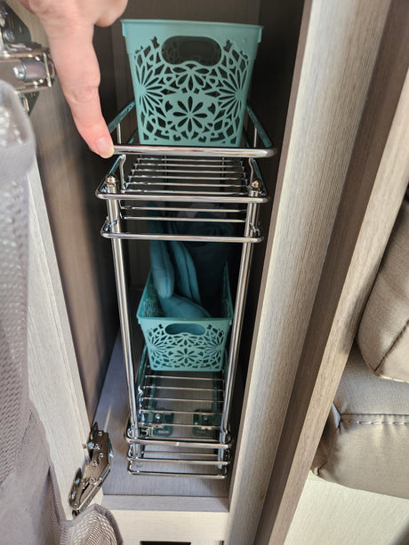 RV rental: Finger points to a chrome pull-out rack with teal decorative bins, maximizing under-cabinet storage.