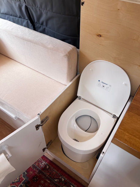 Compact RV rental interior featuring an ingenious Separett composting toilet tucked beside a cozy seating area. Ideal for van life.