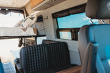 Inside an RV rental: a bright camper van interior with an elevated bed, black quilted seats, and a large window.