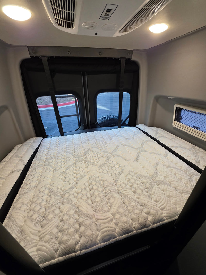 Inside an RV rental: a plush, quilted mattress fills the rear sleeping area, flanked by windows. Ceiling features lights & AC. — photo 9
