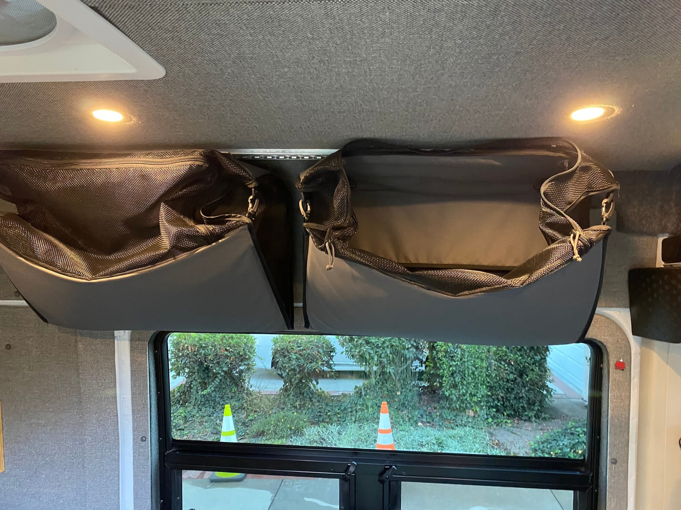 Overhead mesh storage bags in an RV rental interior, illuminated by ceiling lights, with a view of greenery outside the window. — photo 11
