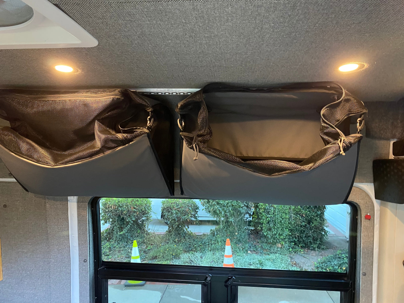 Overhead mesh storage bags in an RV rental interior, illuminated by ceiling lights, with a view of greenery outside the window.